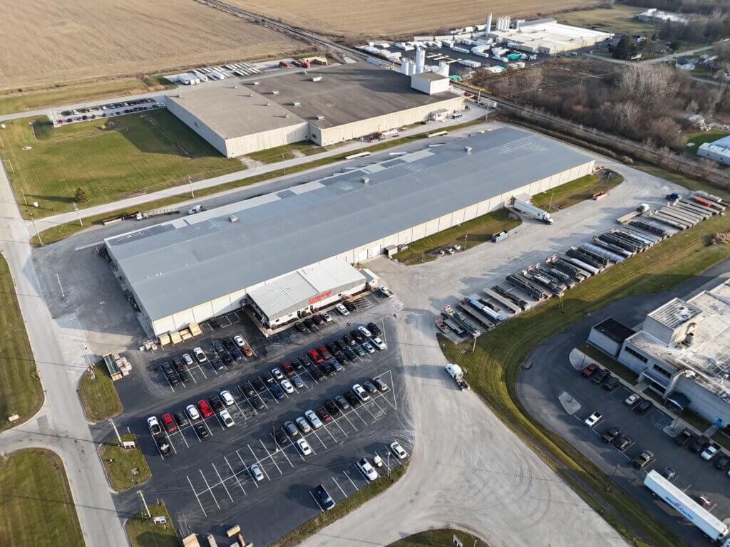 Aerial view of the Chief's facility in Rensselaer, Indiana, showing a large warehouse, semi-truck lot, office entrance, and surrounding farmland.
