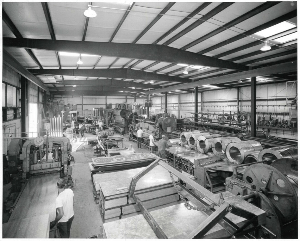 Black and white photo of Chief Agri’s fully automated grain bin manufacturing plant in Rensselaer, Indiana, with workers and large industrial machinery.