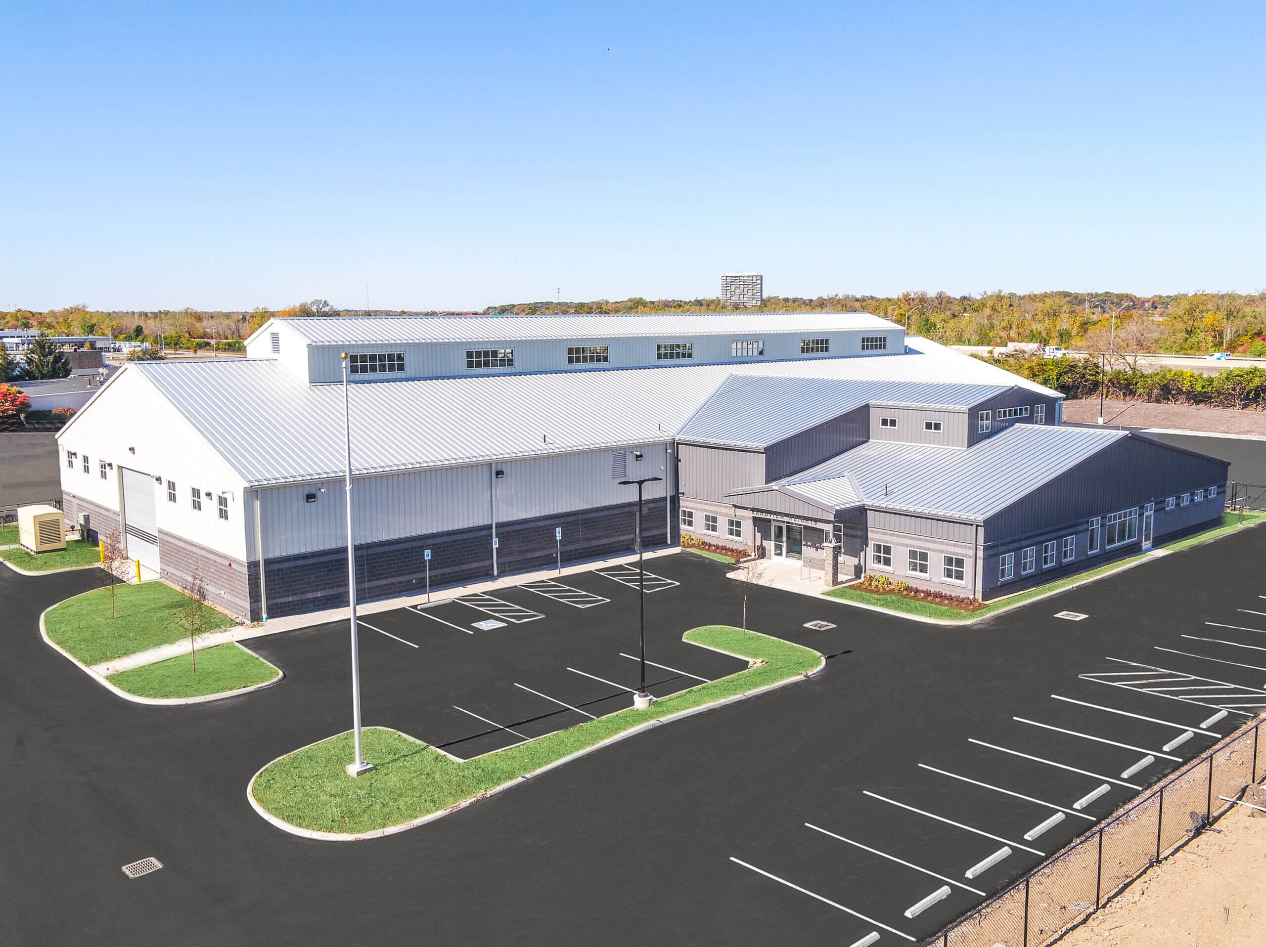 A large, completed manufactured metal building with light gray panels and a dark brick wainscot, featuring office space and a high-clearance industrial section.