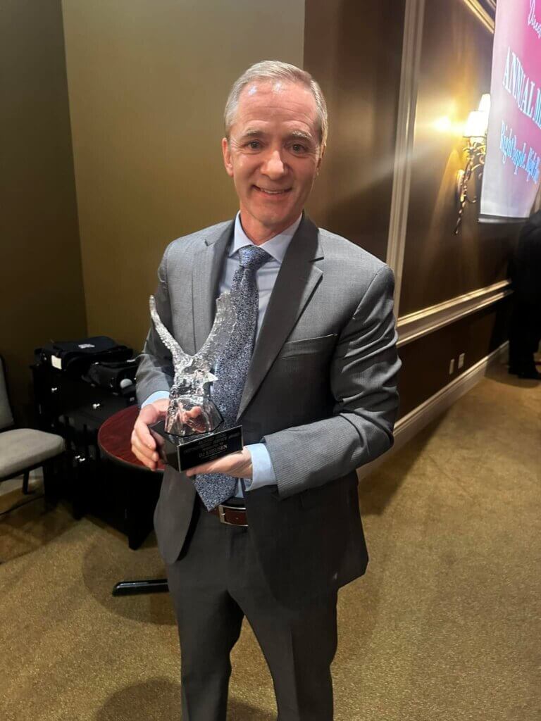 DJ Eihusen stands smiling with award in hand after receiving the Distinguished Service Award from the Grand Island Chamber of Commerce.